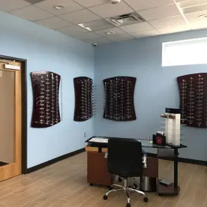 A room with a wooden floor, blue walls, and a desk with a chair and glasses on display, along with a window and surveillance camera on the ceiling.