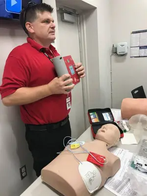 A man in a red shirt is standing in front of a mannequin wearing a red first aid kit on its chest.