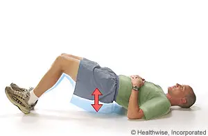 A man lies on a mat on a white floor with his legs bent and feet on the floor, wearing a green shirt, gray shorts, and sneakers, and a red arrow points upward near his left knee.