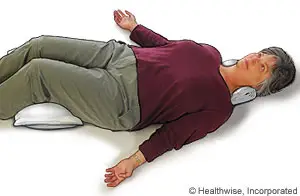 Illustration of a woman lying down on her back with her arms extended above her head, wearing a maroon shirt and green pants, possibly engaging in a physical therapy exercise with a pillow under her head and headphones on, on a white background. The image has a watermark that reads Healthwise, Incorporated.