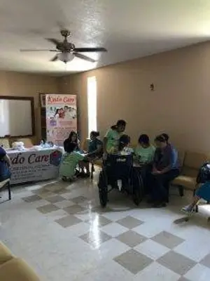 A group of people sitting in a room with chairs and a table, while one person is standing and another is using a wheelchair.