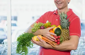 A man holding a basket full of fresh fruits and vegetables in a supermarket.