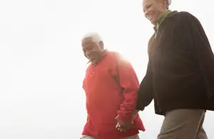 An elderly couple smiling and holding hands while walking in the sunlight.