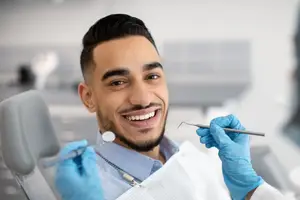 A dentist with a smiling face is holding dental tools in his hands.