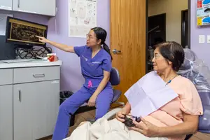 A woman in blue scrubs is showing a dental X-ray to an elderly woman in a pink shirt in a dental clinic.
