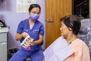 A dental hygienist discusses dental care with a patient while holding a model of teeth in a dental clinic.