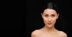 Portrait of a woman with black hair looking directly at the camera with a black background