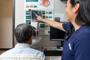 An older man getting his eyes checked at the optometrist with the help of a woman wearing a blue shirt