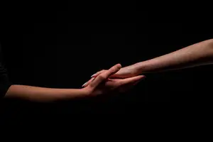 Two hands holding each other in a dark room with a black background.