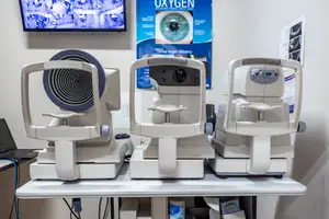 Three ophthalmoscopes on a table with a television and a poster in the background