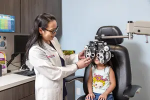 A female doctor is examining a young girl's eyes using an ophthalmoscope in an eye clinic.