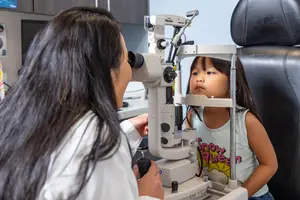 A woman doctor examining a young girl's eyes using a slit lamp in a clinic