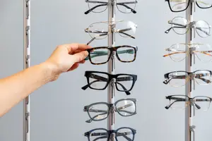 A hand is holding a pair of Gucci glasses in a store, surrounded by other Gucci glasses on display.