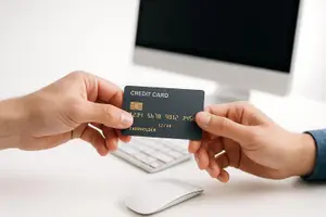 Two hands are holding a credit card with the words credit card on it in front of a monitor and keyboard.