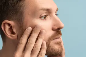 A man touching his face with a blue background