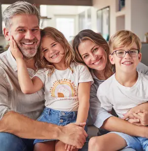 A family of four smiling and posing for a picture with the father's hand on the daughter's cheek