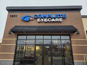 A storefront with a black awning, a blue logo reading 'Complete Eyecare', and a glass door reflecting the surroundings.