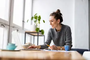 Woman sitting at a desk working on a laptop with a smile on her face.