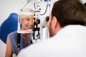 A smiling woman is having her eyes examined by a male doctor in a white coat.