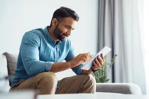 A man sitting on a couch and looking at a tablet with a smile on his face