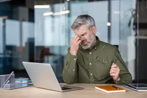 old man with glasses and laptop on desk in office