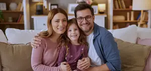A family of three people sitting on a couch, smiling, and looking at the camera.