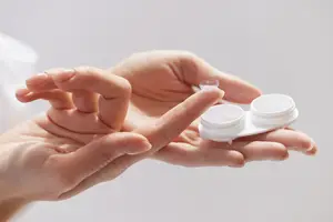 A hand holds a contact lens in a lens case.
