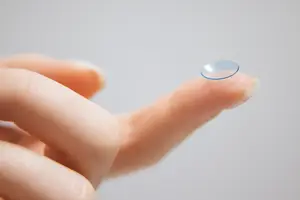 A finger holding a transparent contact lens with a blue outline
