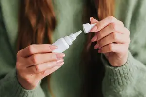 A woman holding a white bottle of eye drops in her hands