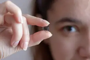 A woman holds a small, transparent contact lens in her hand, examining it closely.