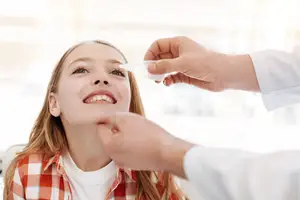 A young girl smiles as a doctor administers eye drops to her eye.