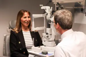 A woman sitting in an optometrist chair while the doctor looks into an ophthalmoscope