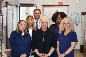 Six people posing for a photograph in an office with a glass cabinet in the background.