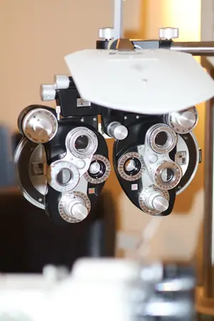 An optometrist's equipment with a white shield is placed on a metal rod and is connected to a cable in an optical shop.