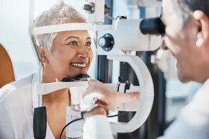 A woman is getting her eyes checked by a doctor in an exam room.