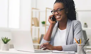 A woman sitting at a desk talking on a cellphone while smiling