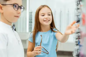 Two children in a store looking at glasses on a display rack