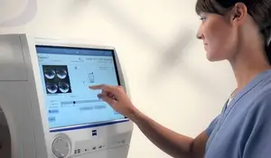 A nurse points at an eye chart displayed on a medical monitor in a clinical setting.