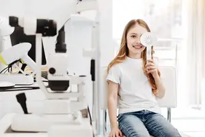 A young girl smiles while sitting in a dental chair, holding a sun-shaped mirror.