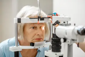 An older woman is looking into an eye exam machine at the doctor's office