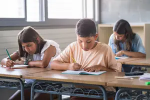 Three children in a classroom writing in their notebooks