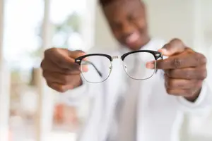 A man holding up a pair of glasses while smiling