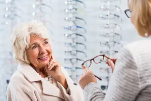 An older woman is trying on glasses in an optical shop with a smiling face