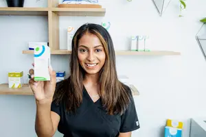 A woman holds a box of supplements and smiles at the camera.