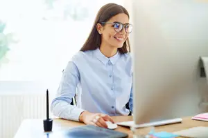A woman sitting at a desk using a computer with a smile on her face