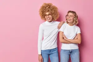 Two women standing next to each other in front of a pink wall