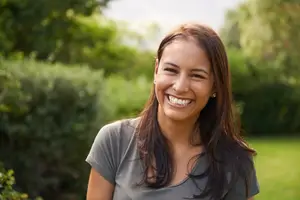 A smiling woman standing in a garden with plants and trees behind her