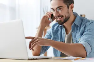 Man using a laptop while talking on a cellphone in an office room