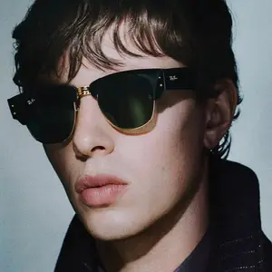 A close up of a man wearing black sunglasses with gold accents and a black jacket