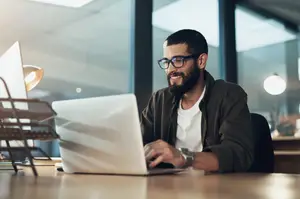 Man sitting at desk using laptop with smile on face